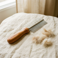 Double-sided dog grooming comb with a beech wood handle and steel pins on cream linen