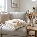 Cream fleece blanket with a soft printed golden retriever portrait, folded on a linen sofa